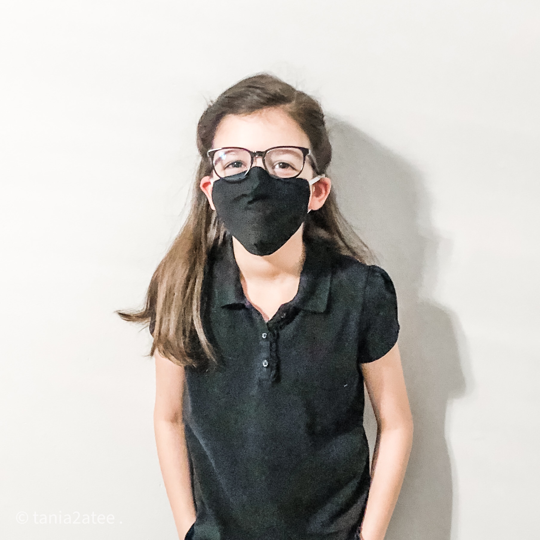 girl posing for camera with hands in her pockets wearing black top and pants, glasses and black face mask